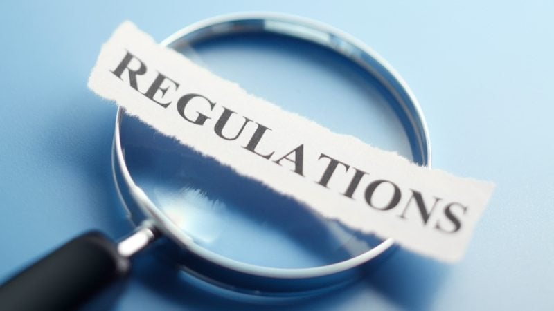 Magnifying glass focusing on the word “regulations” on blue backgroun