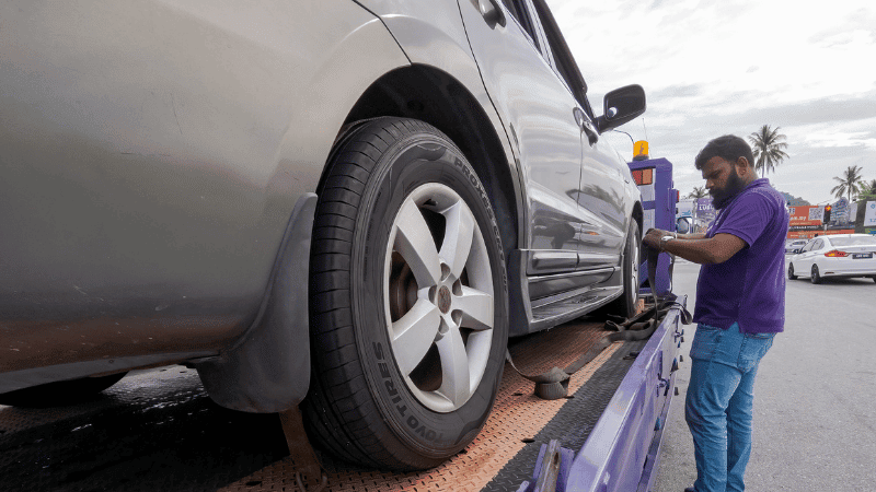 A tow truck operator securing a vehicle during a repossession process.
