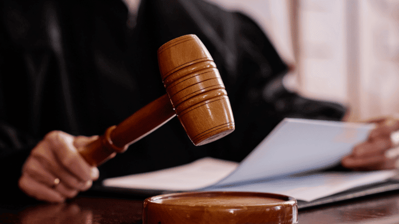 A judge holding a gavel and reviewing legal documents in a courtroom setting.