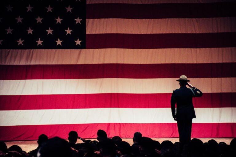 man standing on stage facing an American flag