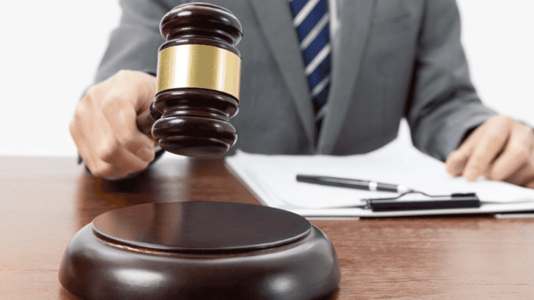 A judge holds a gavel while seated at a desk.