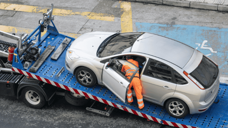 A damaged car being loaded onto a tow truck by a worker in orange attire.