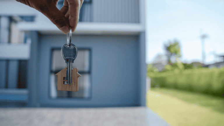 A hand holding house keys in front of a modern home.
