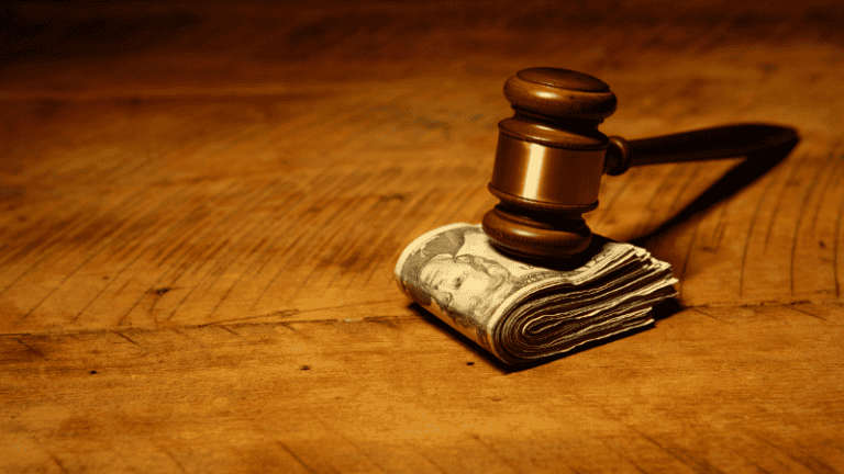 A gavel resting on a stack of money on a wooden surface.