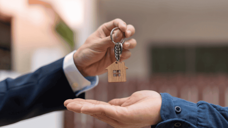 A person handing over a house-shaped keychain to another person, symbolizing property transfer or rental.
