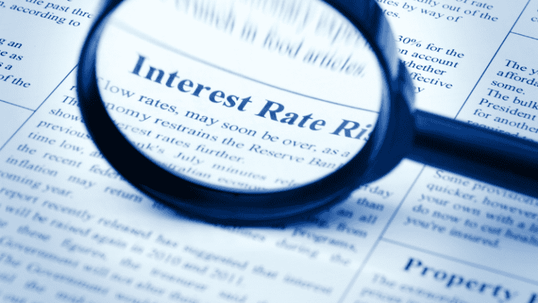 A magnifying glass focusing on a newspaper headline about interest rate rises, symbolizing financial scrutiny and economic analysis.