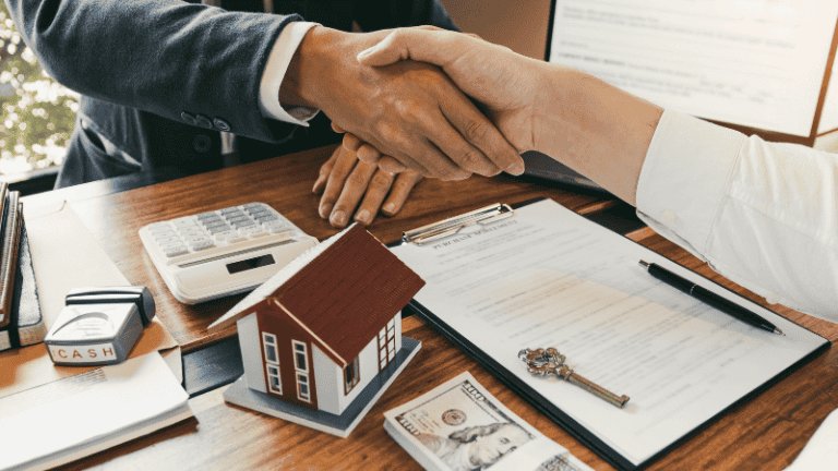 A handshake over a table with a miniature house, keys, and cash, representing a property deal or rental agreement.