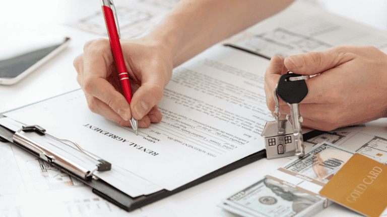 A person signing a rental agreement while holding house keys, symbolizing a lease transaction.