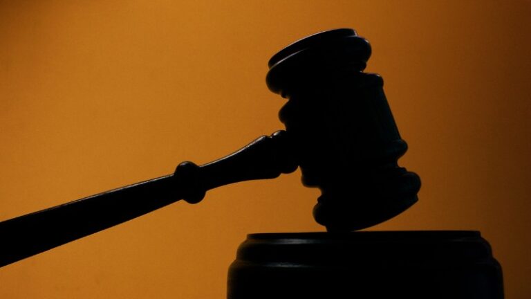 A silhouette of a gavel against an orange background.