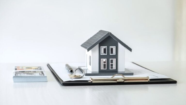 Model house on clipboard with pen, keys, and money