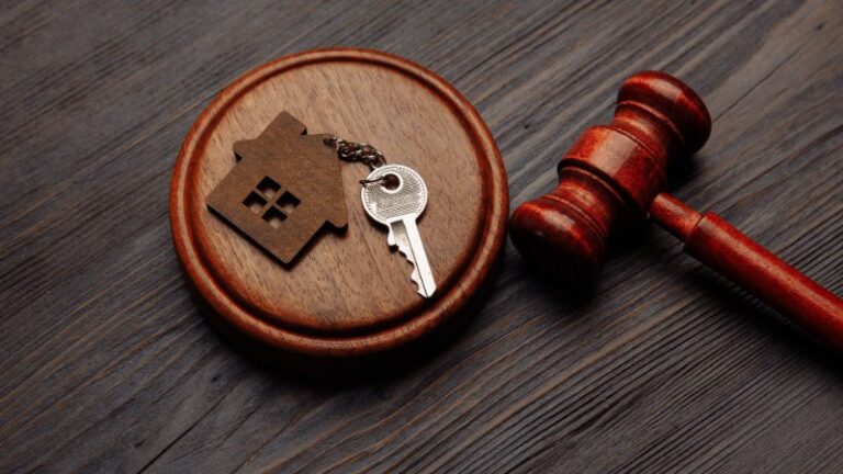 Wooden gavel beside house key on judge’s block.