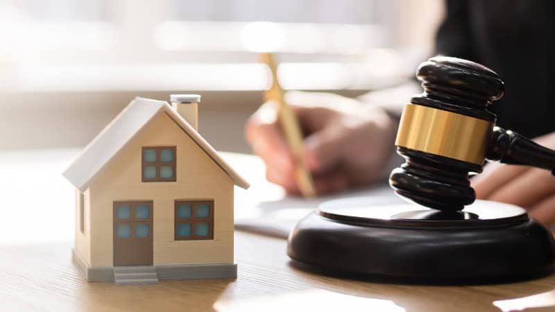 Wooden house model and gavel with person writing