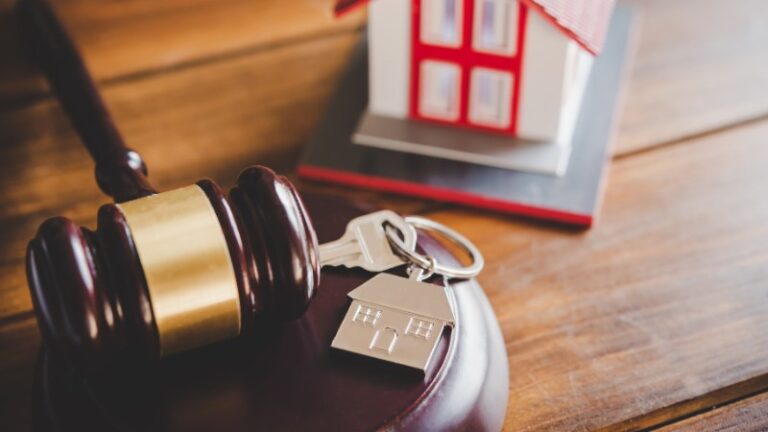 Gavel and house key with miniature home in background.
