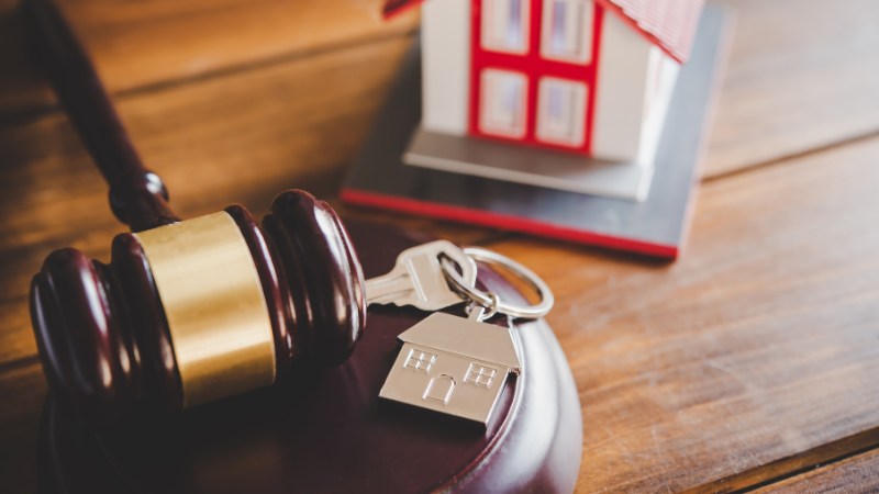 Gavel and house key with miniature home in background.