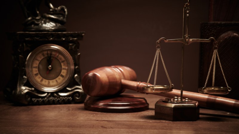 A judge’s gavel and balance scale on wooden table.