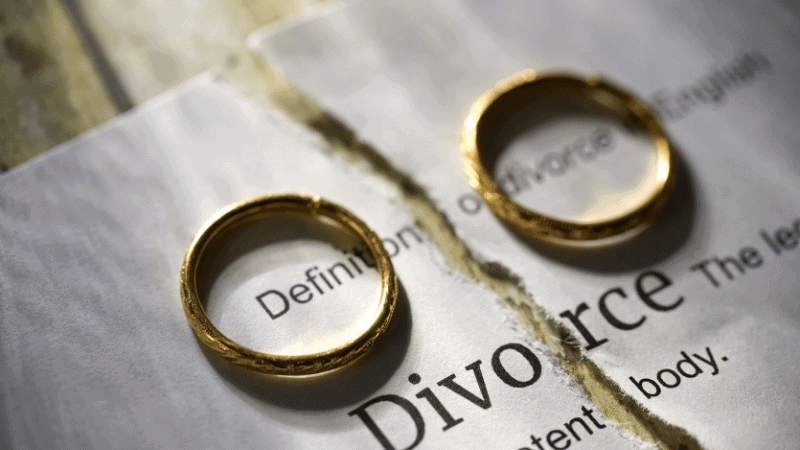 Two wedding rings placed on a torn page with the word “Divorce,” symbolizing the legal end of a marriage.