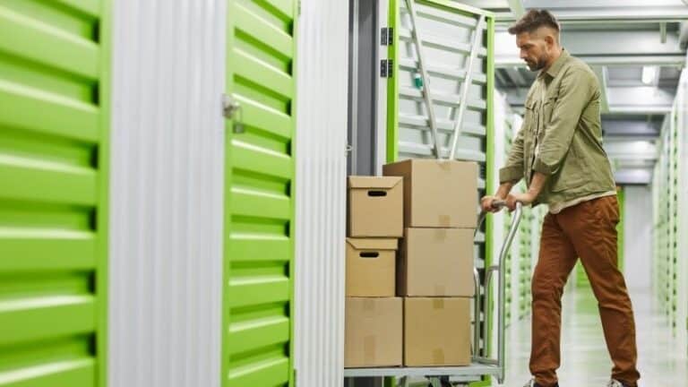 Man moving cardboard boxes into a bright green storage unit.