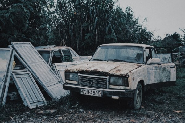 Abandoned rusty car parked beside metal scrap outdoors.