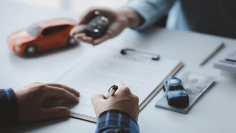 A person completing vehicle title documents with car keys on a desk during the abandoned vehicle title process.