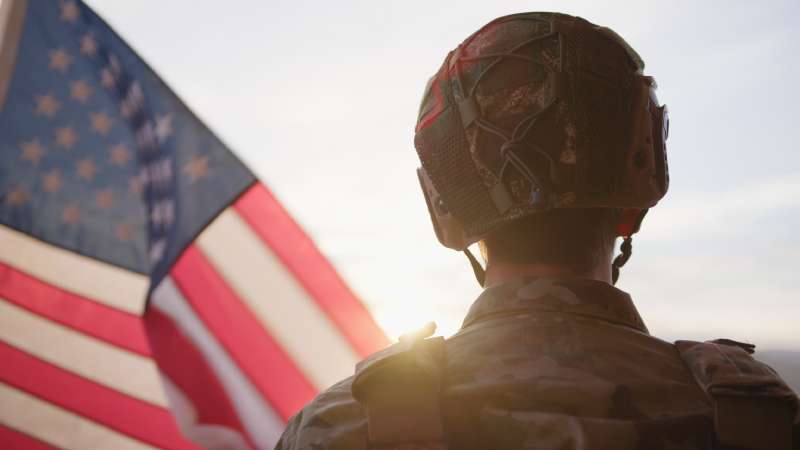 U.S. Servicemember Standing With American Flag Representing SCRA Military Status Protection