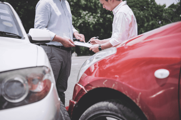 2 men holding a clipboard in front of crashed cars